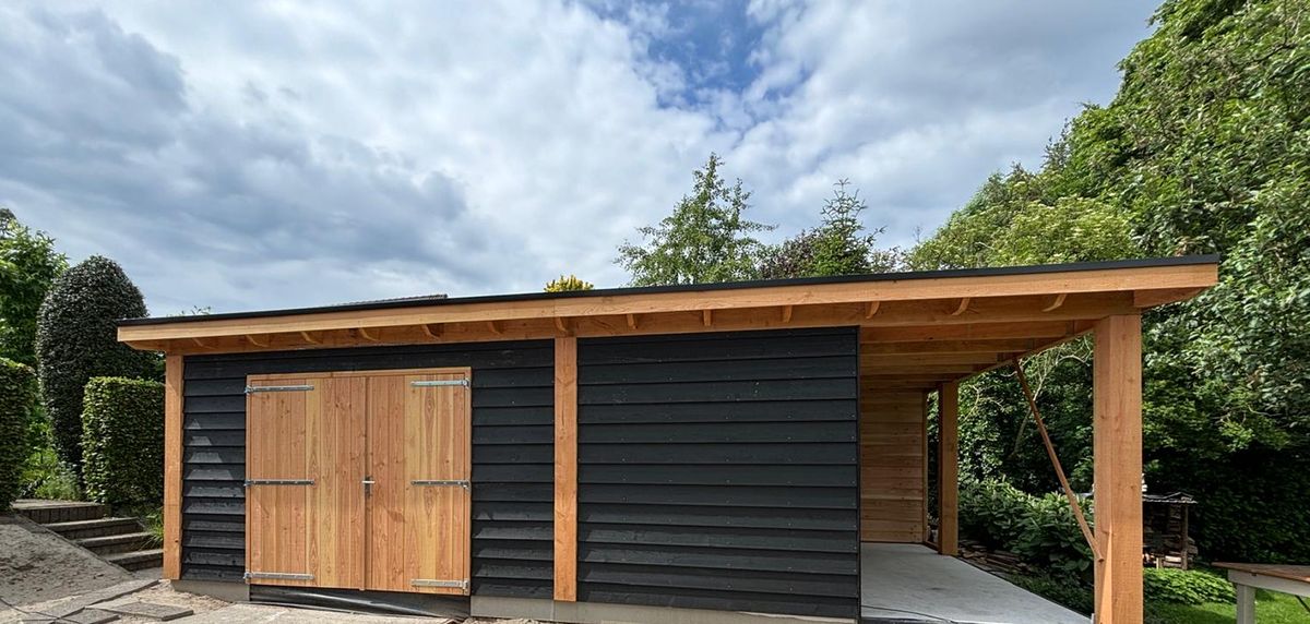 Schuur met zwarte gevelbekleding en een overkapping van Douglas hout